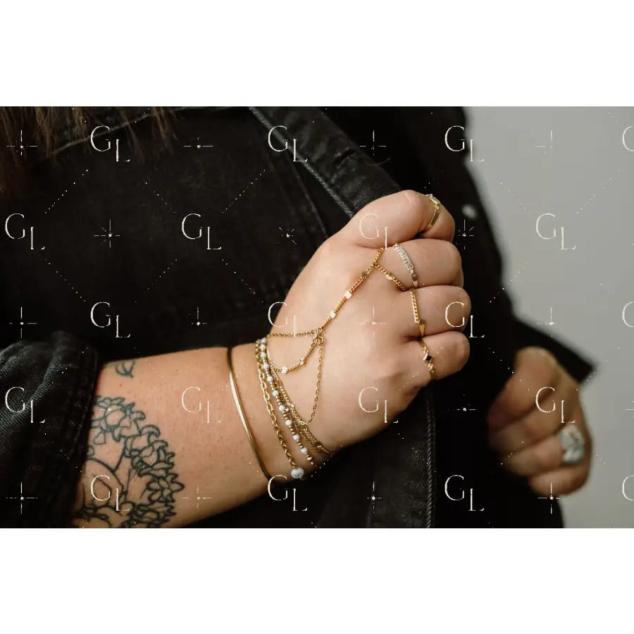 Hand with gold jewelry and tattoos wearing a black jacket