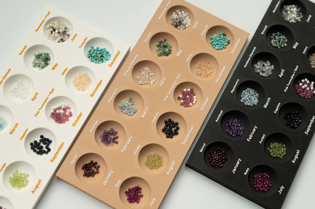 Three trays of gemstones arranged in a grid pattern on a light gray background