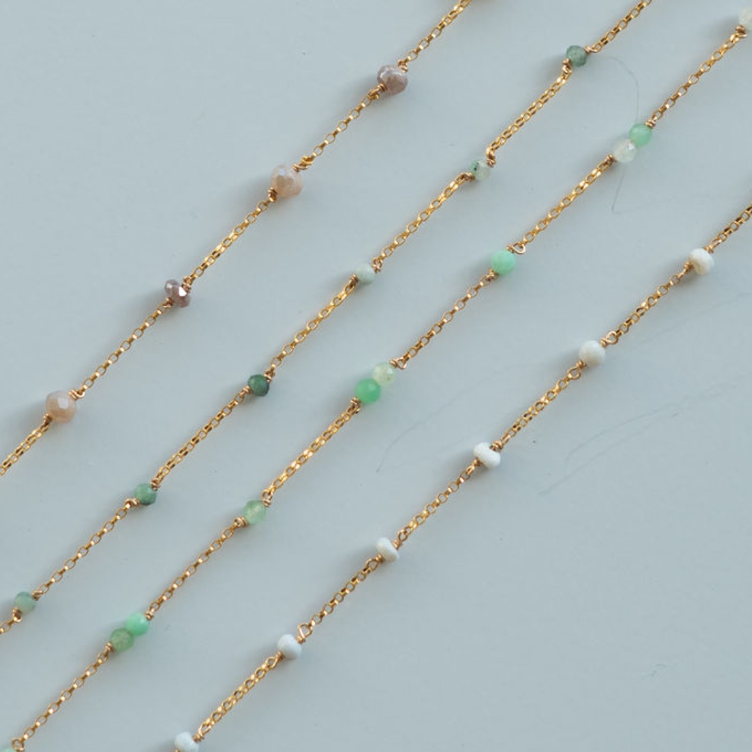 Gold chain necklaces with small beads on a light gray background