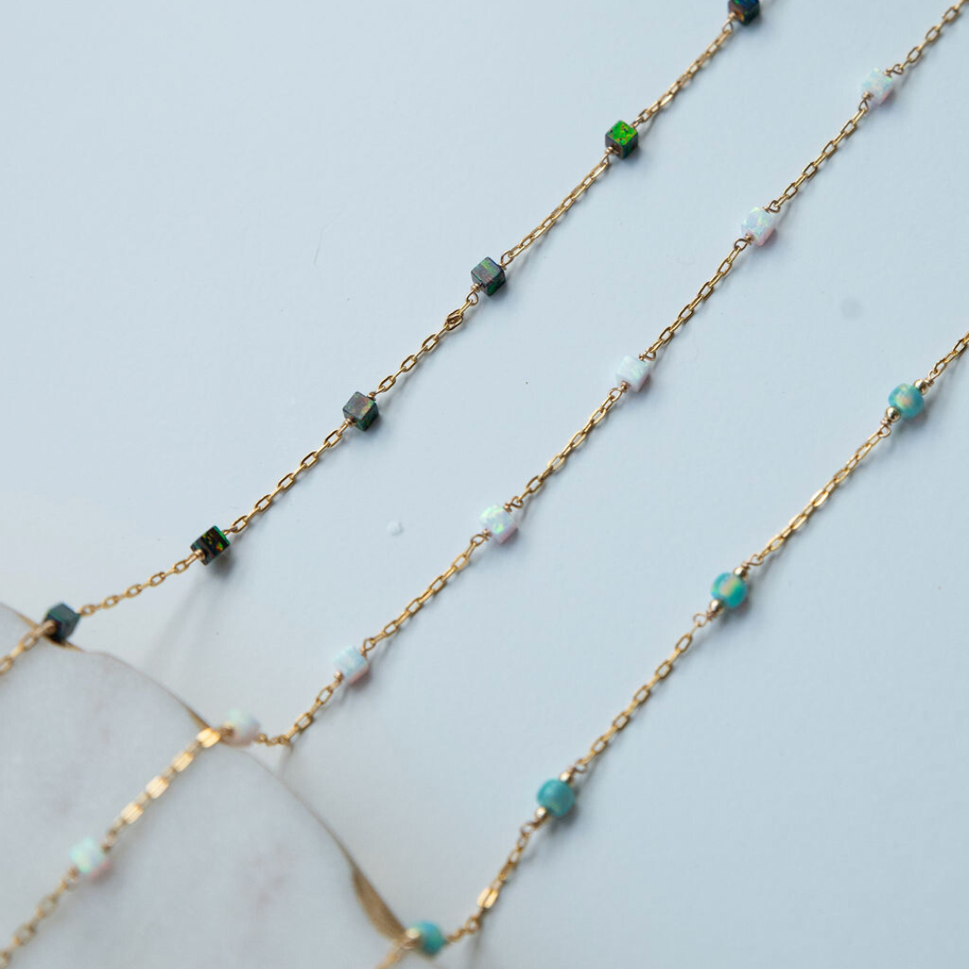 Gold chain necklace with green and blue gemstones on a light blue background