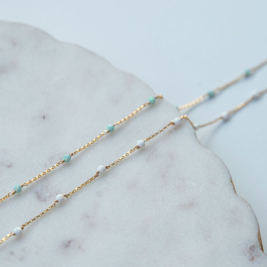 Two gold necklaces with opal blue  and white beads on a marble surface