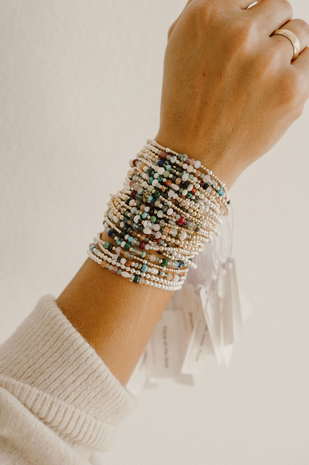Hand wearing multiple beaded bracelets on a neutral background