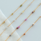 Gold chain necklaces with small colored beads on a light background