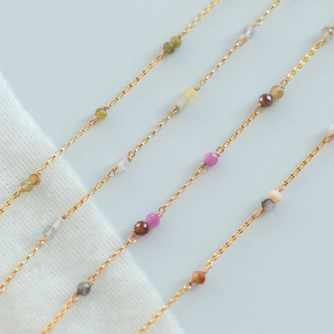 Gold chain necklaces with small colored beads on a light background