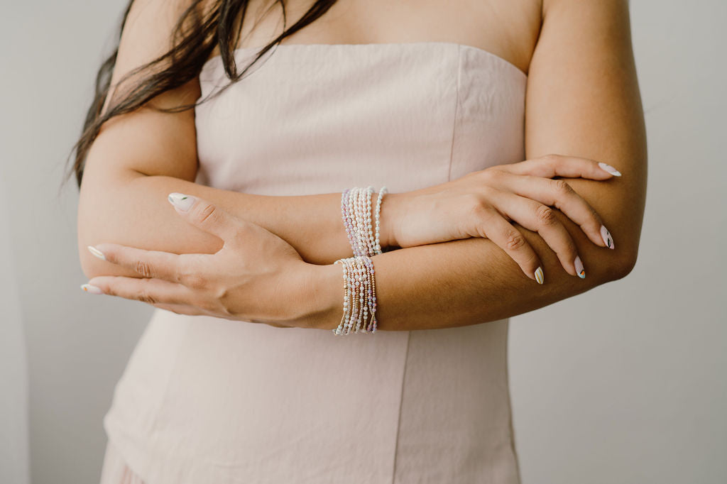 Woman wearing multiple pearl bracelets on her wrist with a neutral background