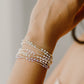 Close-up of a wrist wearing multiple pearl bracelets on a neutral background