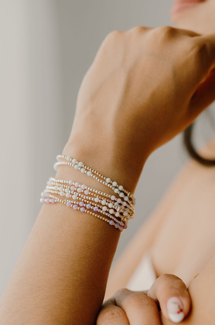 Close-up of a wrist wearing multiple pearl bracelets on a neutral background