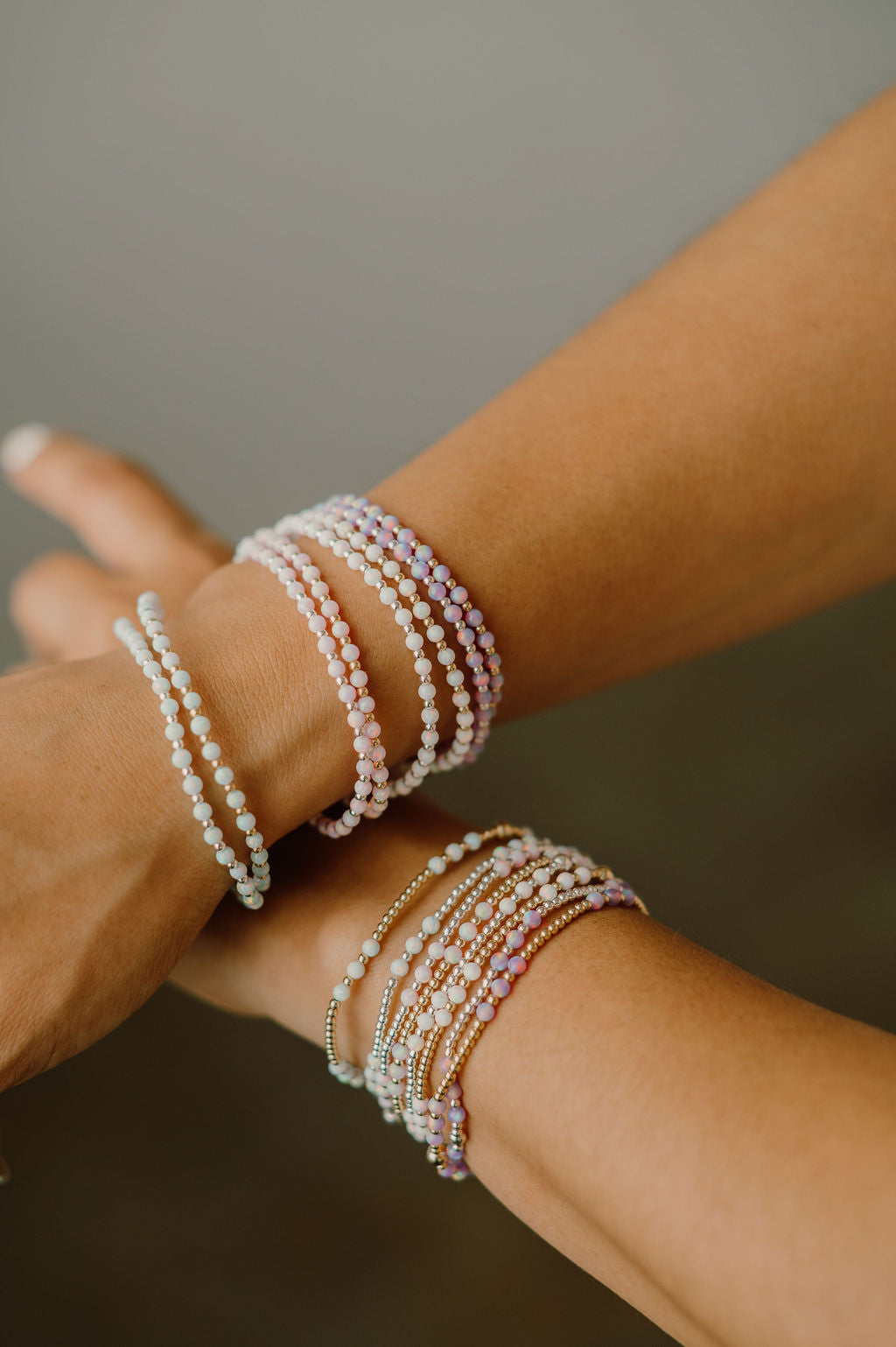 Close-up of a person's wrist wearing multiple pearl bracelets on a neutral background