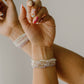 Close-up of a wrist with multiple pearl bracelets on a neutral background