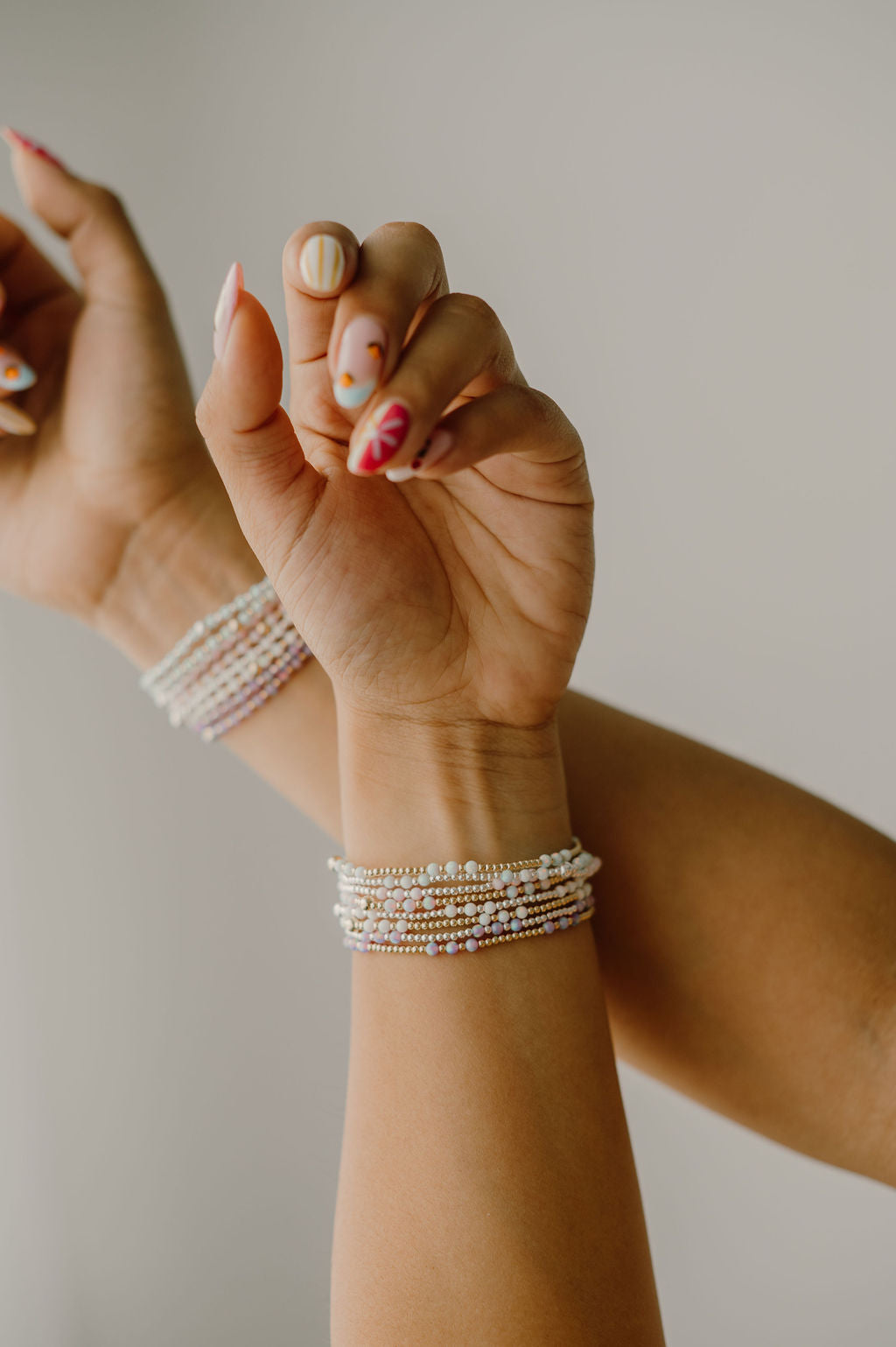 Close-up of a wrist with multiple pearl bracelets on a neutral background