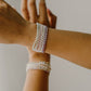 Two arms with pearl bracelets on a neutral background