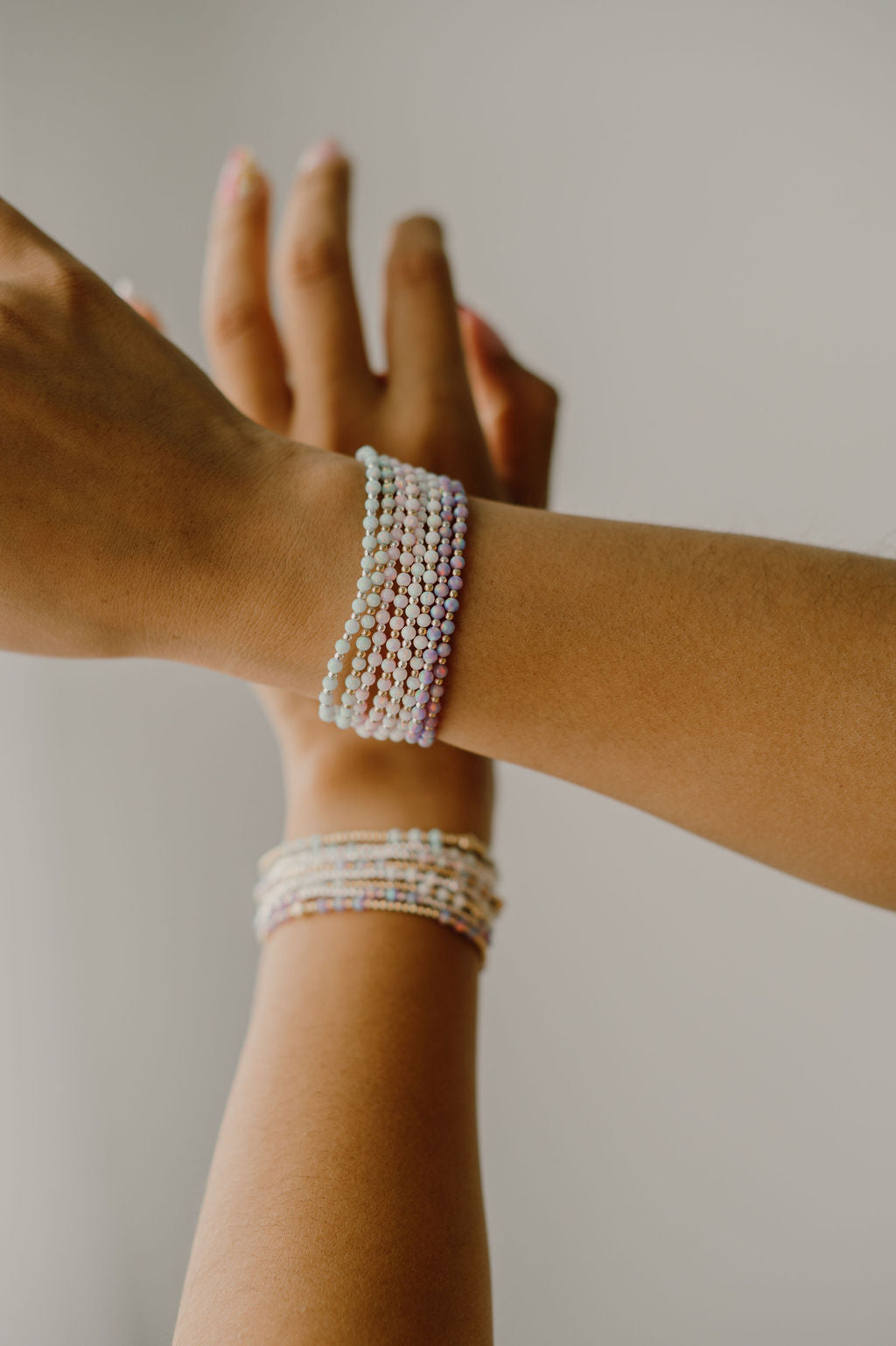 Two arms with pearl bracelets on a neutral background