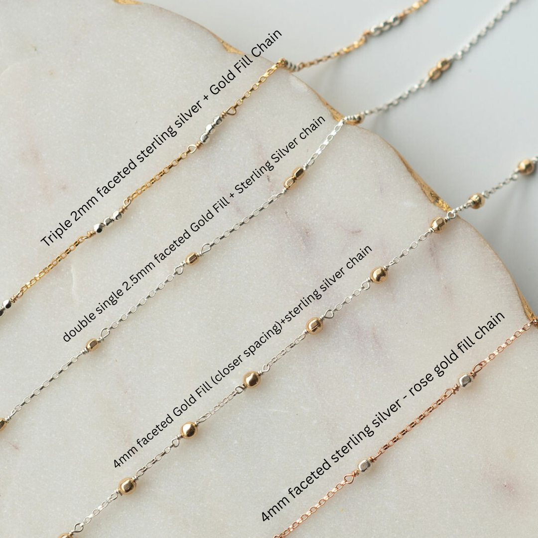 Collection of gold and silver chains on a marble surface with labels.