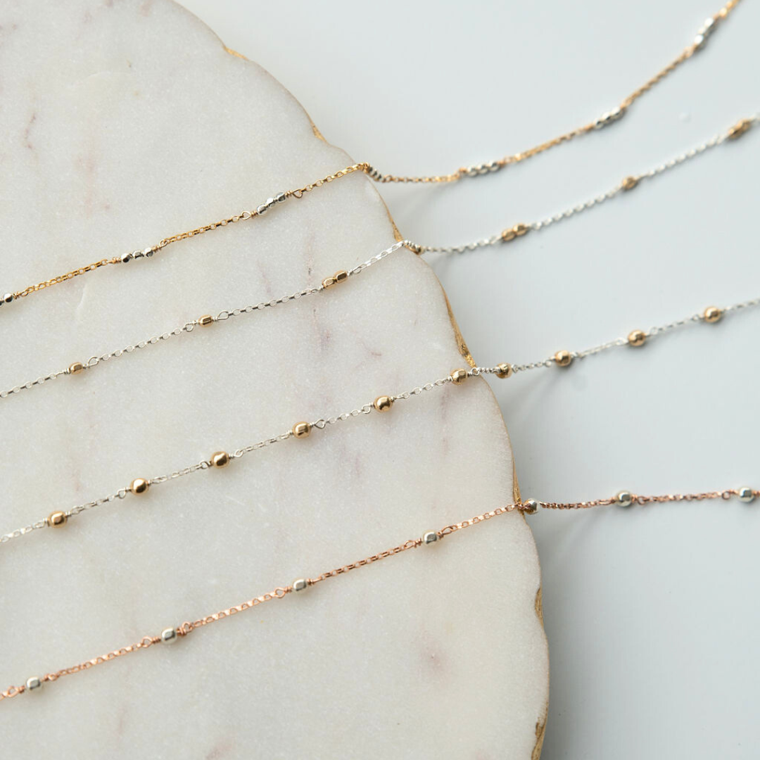 Three delicate gold fill necklaces on a marble surface