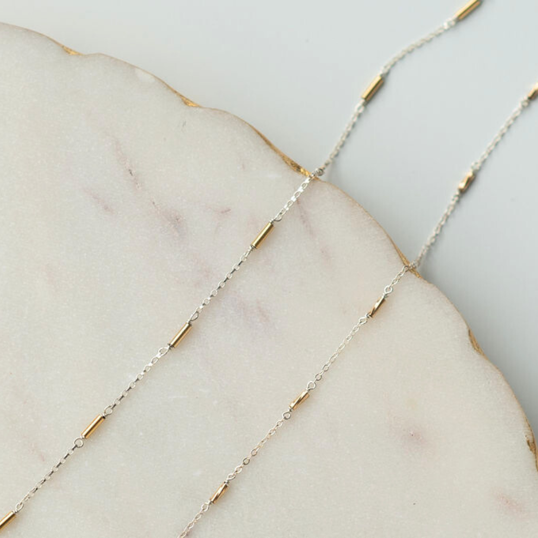 Close-up of a delicate gold and silver chain on a marble surface