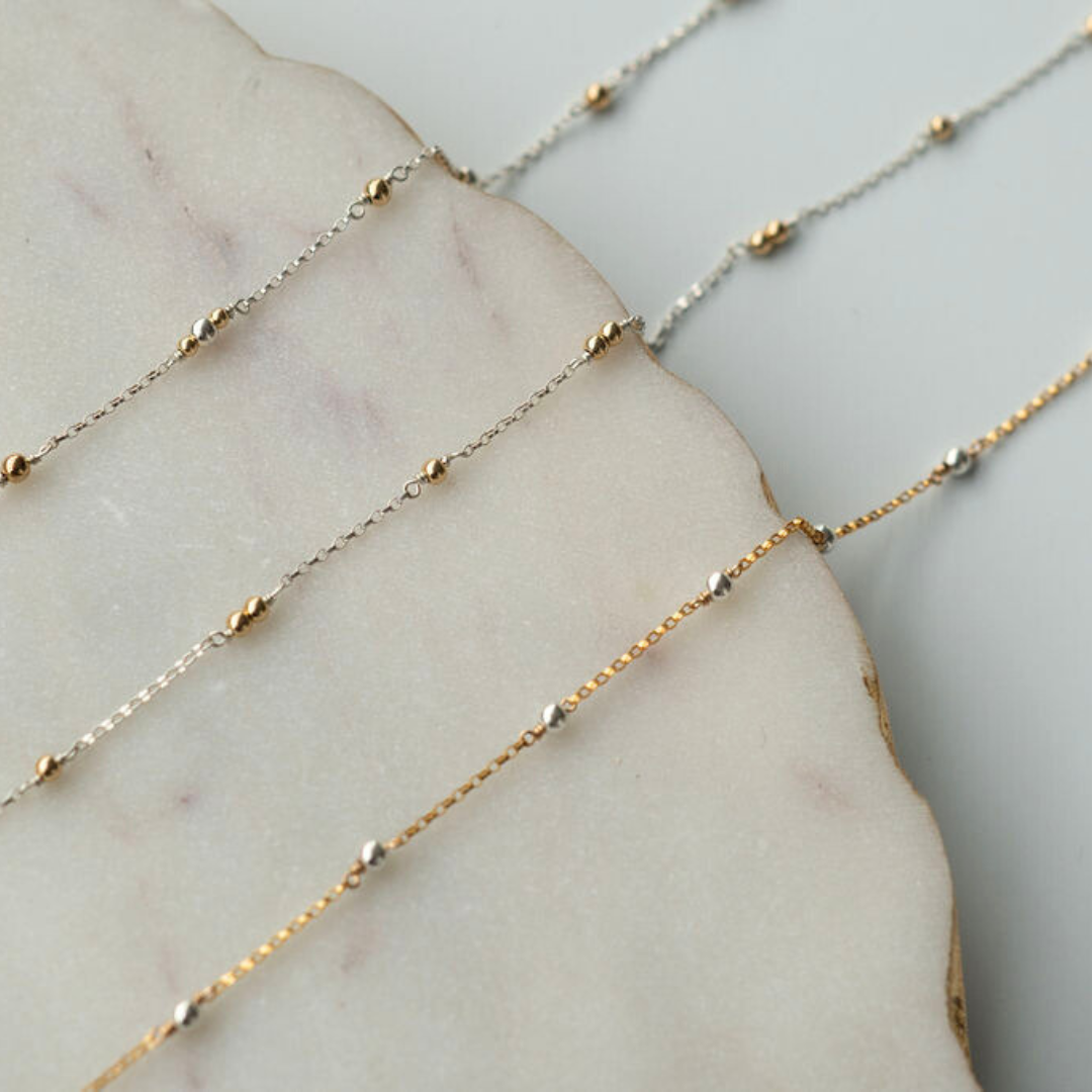 Gold and silver beaded necklaces on a marble surface