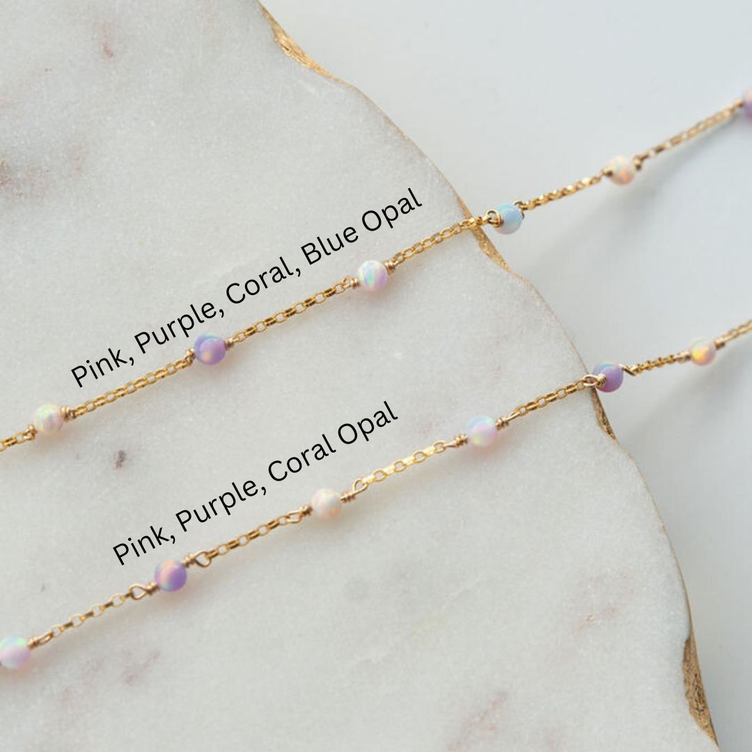 Two gold necklaces with pink, purple, and coral opal beads on a marble surface.