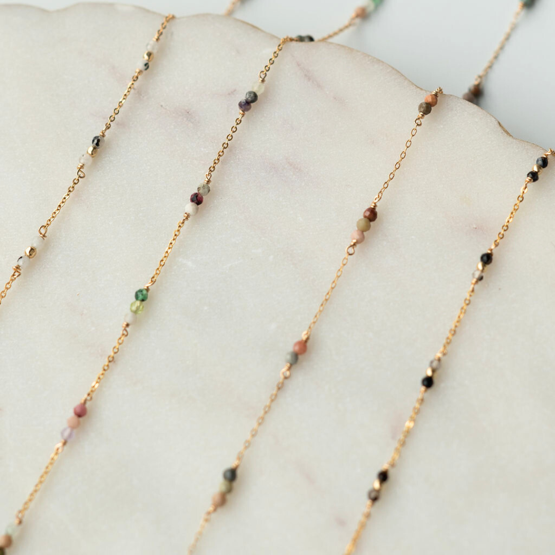 Gold necklaces with small beads on a marble surface