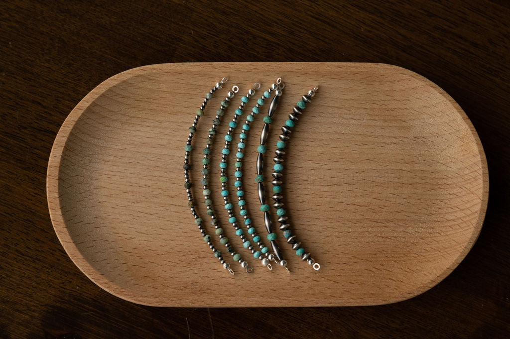 Set of silver and turquoise beaded bracelets on a wooden tray