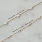 Gold chain with pink opal bar and cloud blue disc opal beads on a light gray background