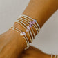 Close-up of a wrist wearing multiple beaded bracelets with heart-shaped charms on a neutral background.