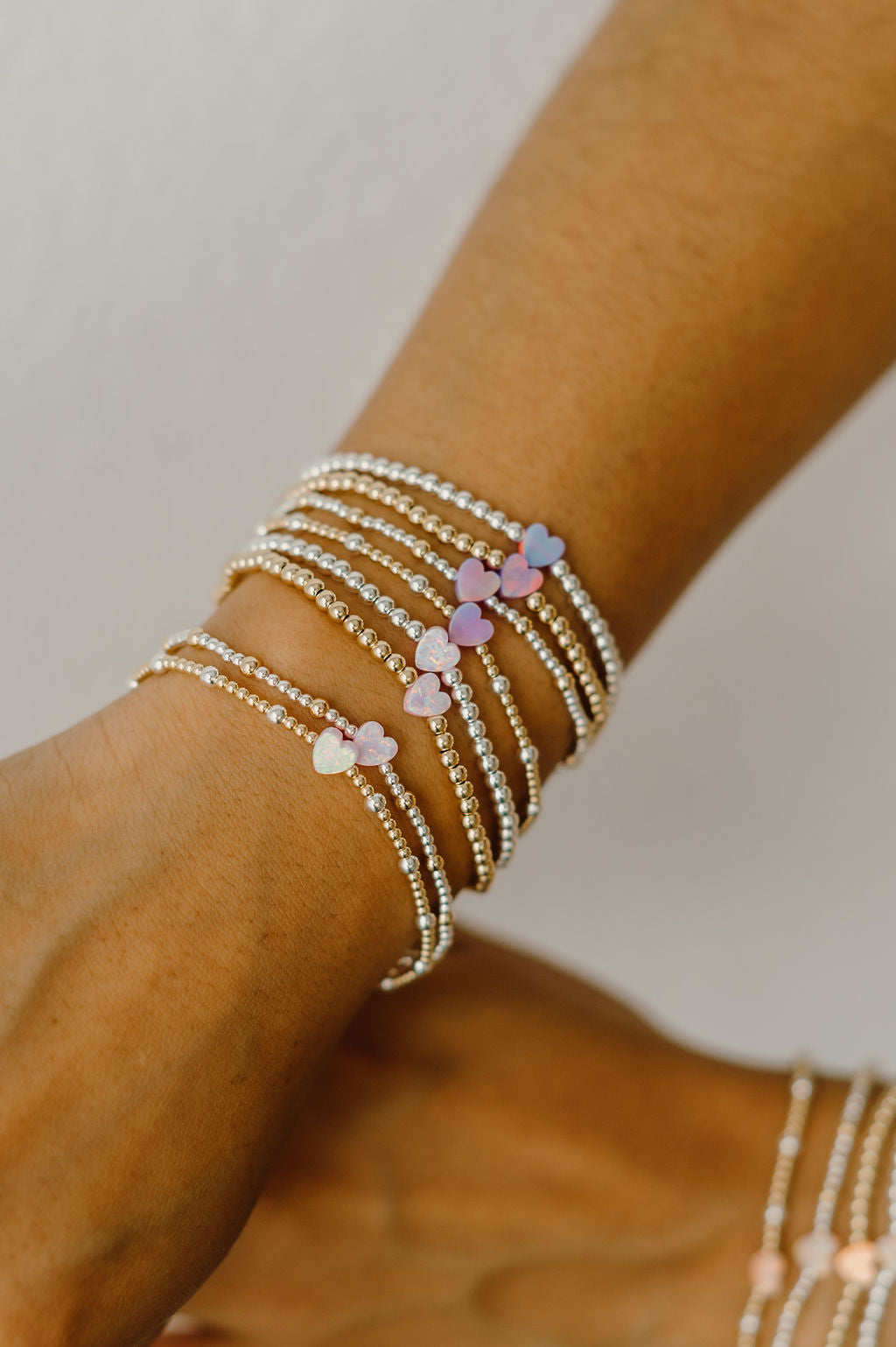 Close-up of a wrist wearing multiple beaded bracelets with heart-shaped charms on a neutral background.