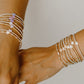 Two hands wearing multiple pearl bracelets on a neutral background