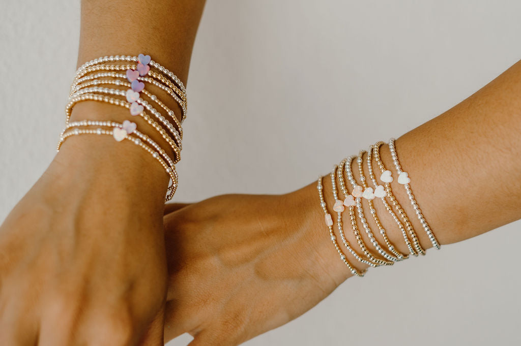 Two hands wearing multiple pearl bracelets on a neutral background