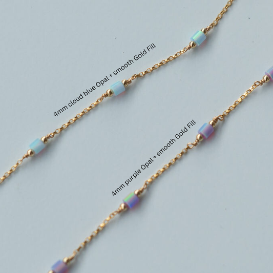 Gold chain necklace with cloud blue and purple opal beads on a light gray background