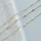 Two gold necklaces with small pearls on a light gray background