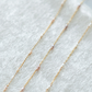 Gold chain necklace with small pearls on a white fabric background