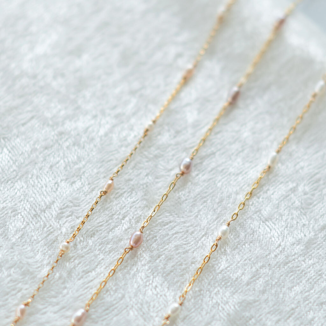 Gold chain necklace with small pearls on a white fabric background