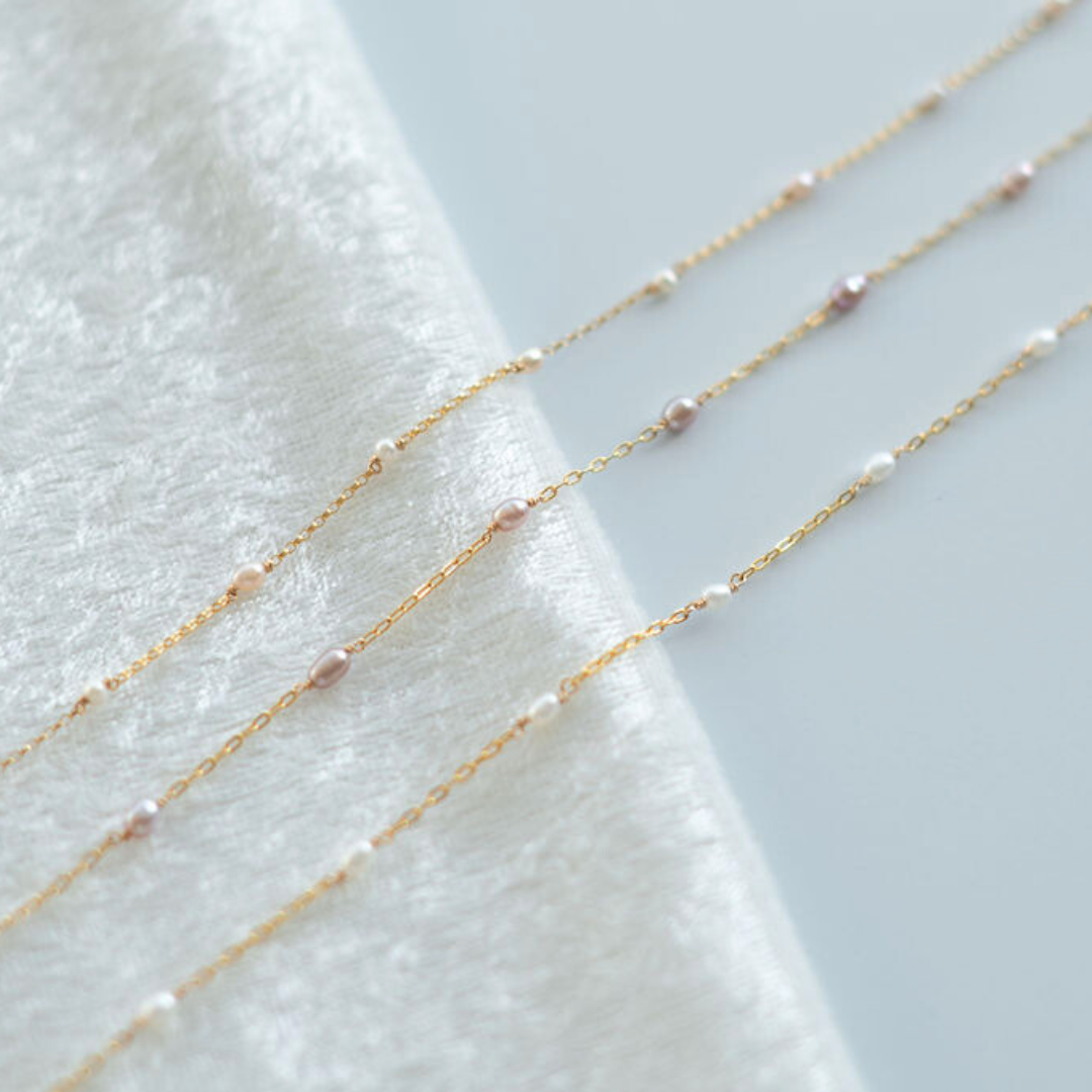 Three delicate gold necklaces with small beads on a textured white surface.
