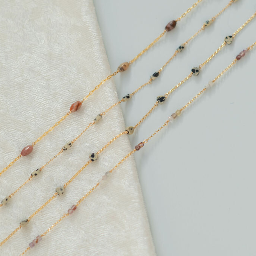 Gold fill chain necklaces with small beads on a textured surface