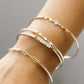 Close-up of a wrist wearing multiple gold Permanent Jewelry Bangle bracelets on a neutral background
