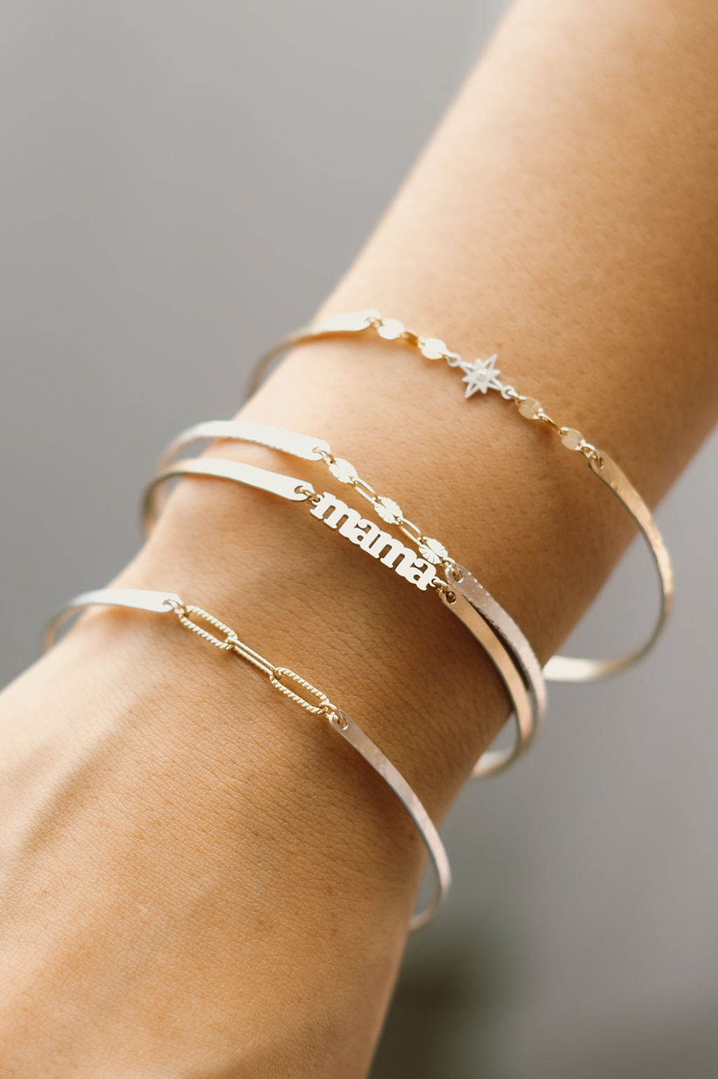 Close-up of a wrist wearing multiple gold Permanent Jewelry Bangle bracelets on a neutral background