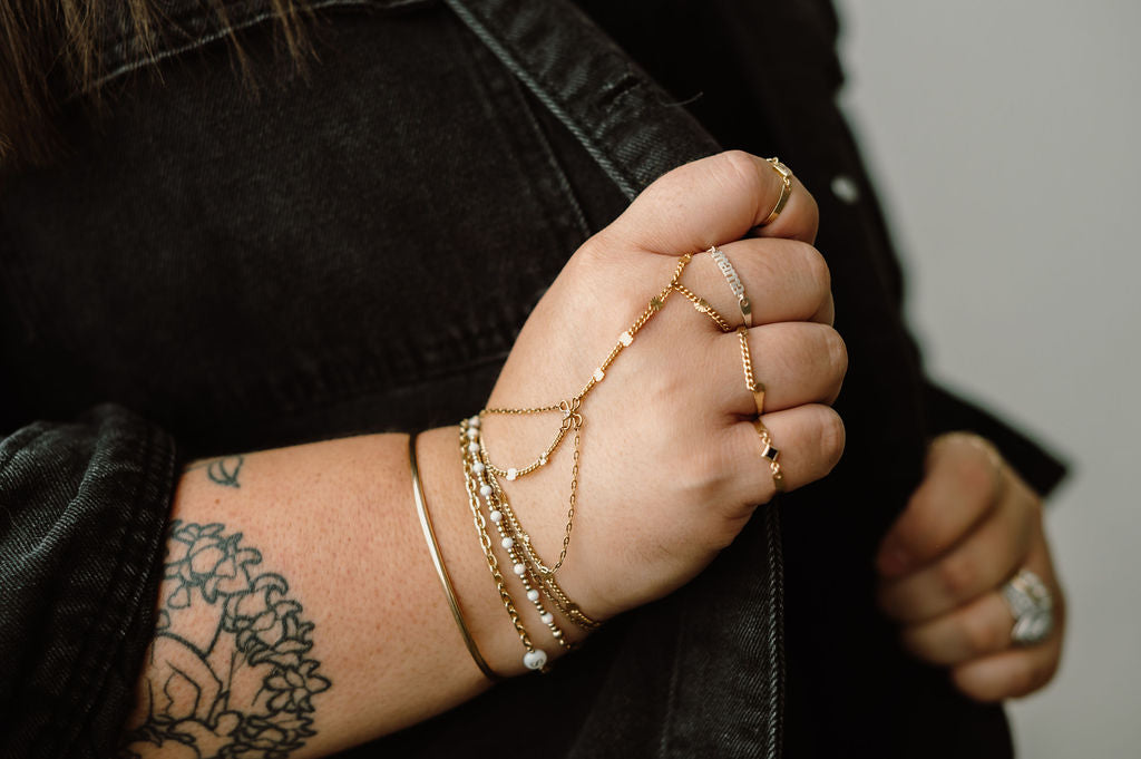 Hand with gold jewelry and tattoos wearing a black jacket