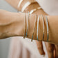 Close-up of a wrist wearing multiple silver bracelets on a neutral background Permanent Jewelry Bangle 