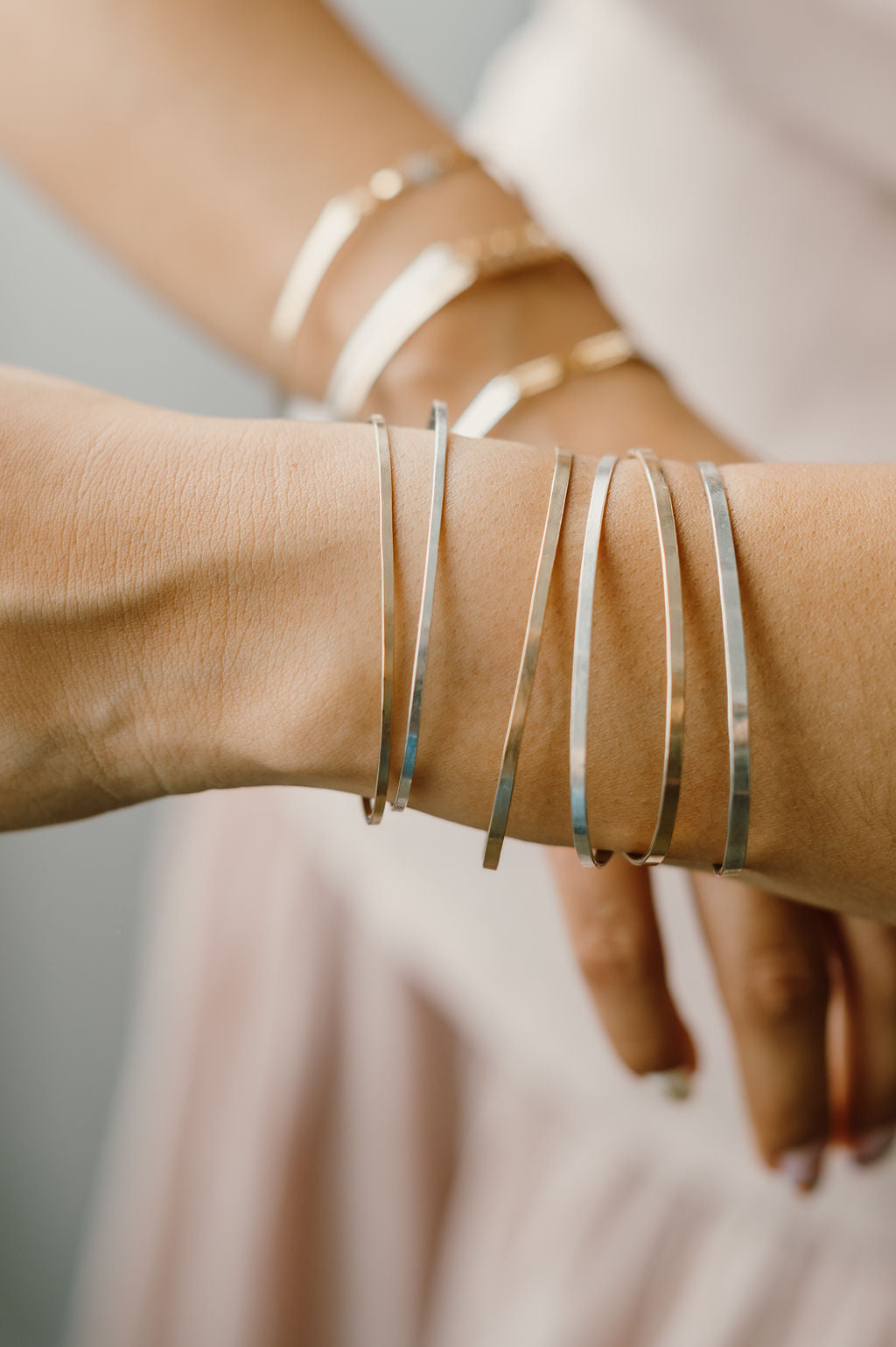 Close-up of a wrist wearing multiple silver bracelets on a neutral background Permanent Jewelry Bangle 