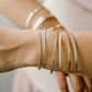 Close-up of a wrist wearing multiple gold bracelets on a neutral background