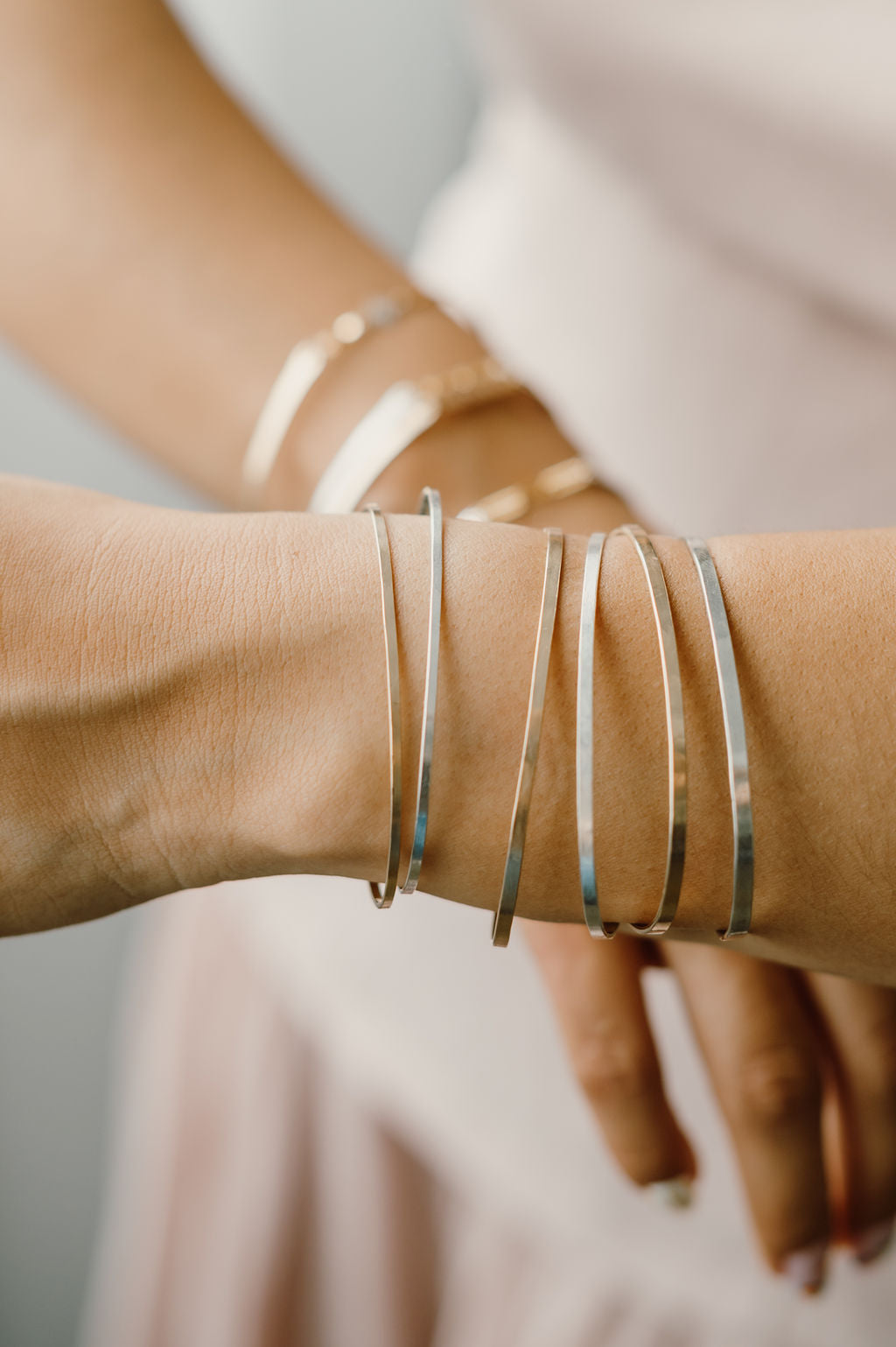 Close-up of a wrist wearing multiple gold bracelets on a neutral background