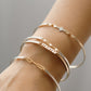 Close-up of a wrist wearing multiple gold and silver bracelets on a neutral background