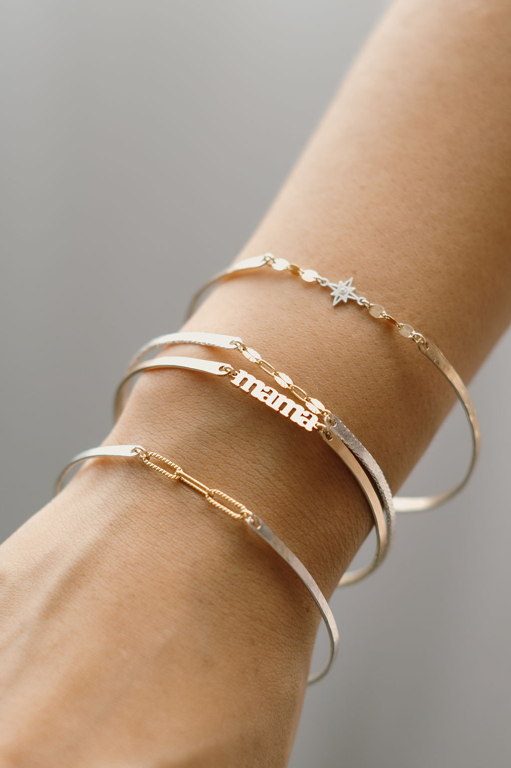 Close-up of a wrist wearing multiple gold and silver bracelets on a neutral background