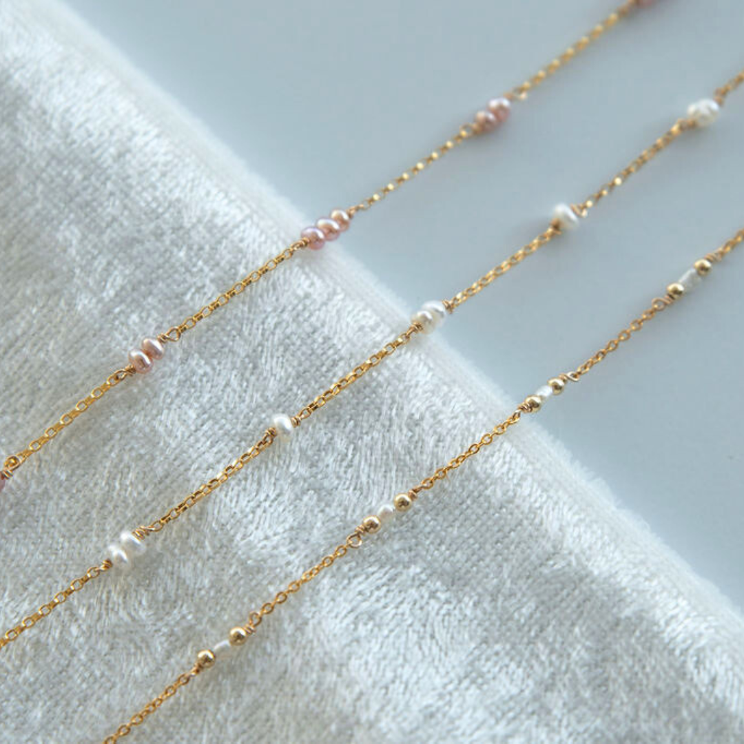 Gold chain necklaces with small pearls on a white towel