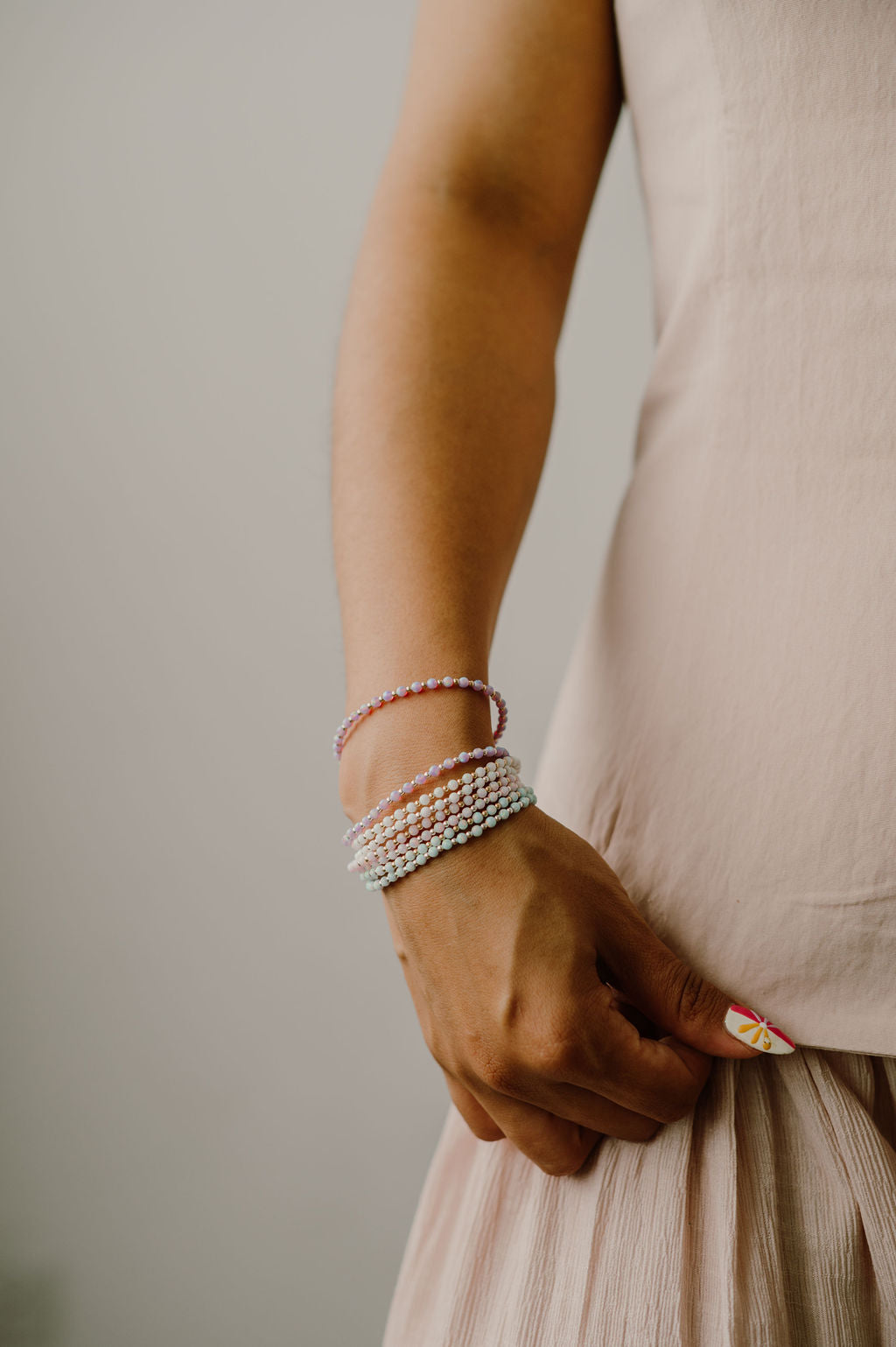 Person wearing multiple opal bracelets on a neutral background