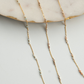 Gold chain necklace with small beads on a light gray surface
