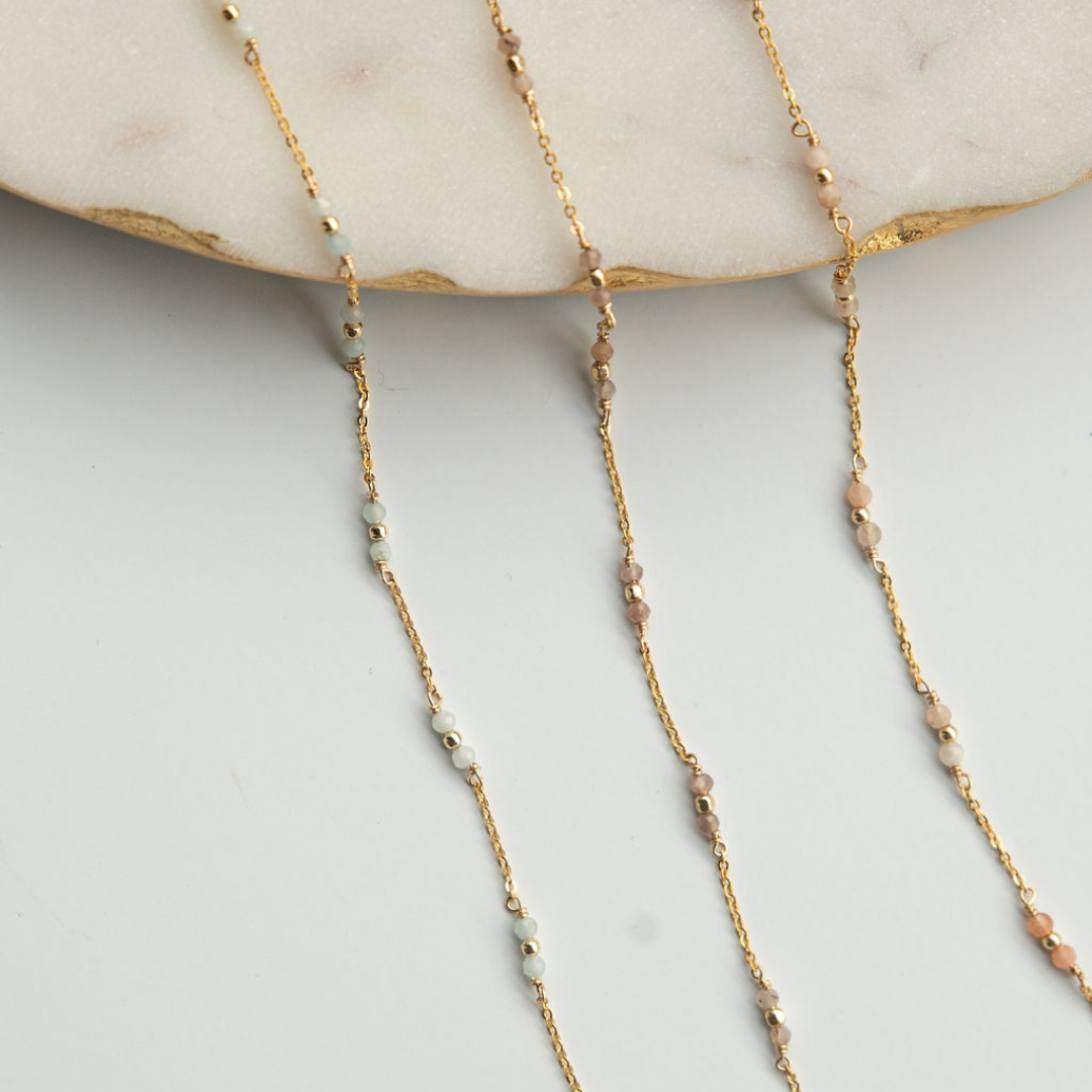 Gold chain necklace with small beads on a light gray surface