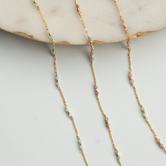Gold chain necklace with small beads on a light gray surface