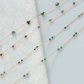 Two delicate beaded necklaces on a light blue fabric background