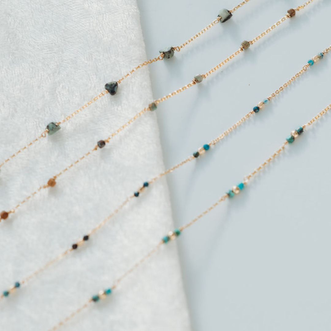 Two delicate beaded necklaces on a light blue fabric background